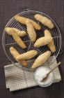 Top view of Zezettes de Sete French pastries on cooling wire rack with icing sugar in jar — Stock Photo