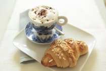 Cappuccino e um croissant de amêndoa — Fotografia de Stock