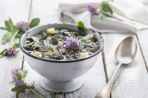 Vegetable soup with clover flowers over wooden surface — Stock Photo
