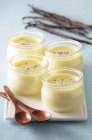 Primo piano vista di quattro bicchieri di crema alla vaniglia con cucchiai di legno sul piatto — Foto stock
