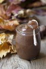 Closeup view of chestnut cream in jar on wooden surface with autumnal leaves — Stock Photo