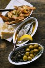 Sardine marinate, scampi fritti e olive in piatti su superficie di legno — Foto stock