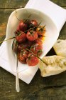 Marinated fried cherry tomatoes; white bread on white plate over towel — Stock Photo
