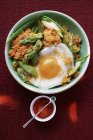Quinoa with ajvar, green asparagus and fried egg in bowl over red surface — Stock Photo