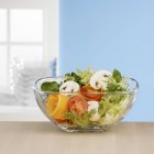 Salad ingredients in glass bowl in front of window — Stock Photo