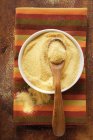 Polenta in bowl with wooden spoon on colored cloth — Stock Photo