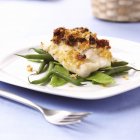 Baked cod on green beans on plate with fork — Stock Photo
