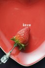 Strawberry on red heart-shaped plate — Stock Photo