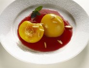 Персики в малиновом соусе на белой тарелке — стоковое фото