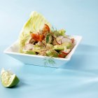 Салат из тунца с овощами на белой тарелке над голубой поверхностью — стоковое фото