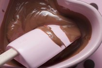 Closeup view of melted chocolate with mixing spoon in heart-shaped dish — Stock Photo