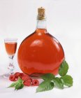 Vista de cerca de la botella y el vaso de licor de frambuesa con frambuesas y hojas - foto de stock