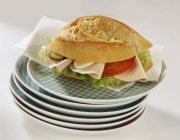 Rolo de pão cheio de frios, ovo, pepino, tomate em placas empilhadas na superfície branca — Fotografia de Stock