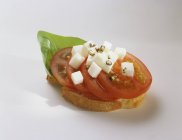 Canap: tomate, mozzarella y albahaca en rebanada de baguette sobre fondo blanco - foto de stock