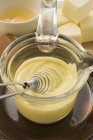 Closeup view of Hollandaise sauce and whisk in small glass pan — Stock Photo