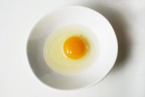 Huevo roto en un tazón blanco - foto de stock
