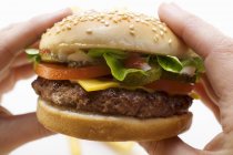 Mani che tengono cheeseburger — Foto stock