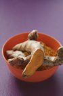 Roots and ground turmeric in bowl — Stock Photo