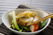 Куриная грудка и креветки на овощах на белой тарелке с деревянными палочками — стоковое фото