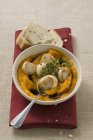 Scallops with pumpkin puree and thyme, white bread  on white plate over red towel — Stock Photo