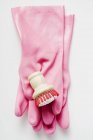 Vista close-up de luvas de borracha rosa e escova na superfície branca — Fotografia de Stock