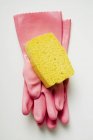 Vue rapprochée du dessus des gants en caoutchouc rose et de l'éponge jaune sur la surface blanche — Photo de stock
