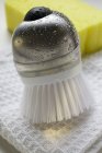 Closeup view of brush with drops of water, tea towel and sponge — Stock Photo