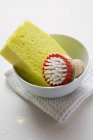 Vista close-up de escova e esponja amarela na tigela na toalha de chá — Fotografia de Stock