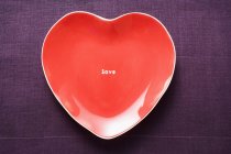 Closeup top view of heart-shaped red plate with word Love — Stock Photo