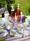 Повышенный вид на чашки, стаканы, напитки и фиолетовый сирень на открытом столе — стоковое фото