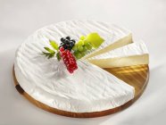 Partly sliced Brie garnished with berries — Stock Photo