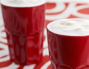 Café con espuma de leche en vasos rojos - foto de stock