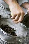 Drenando azeitonas pretas em uma peneira à mão — Fotografia de Stock