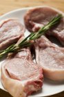 Raw pork chops with rosemary on plate — Stock Photo