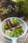 Assorted salad leaves in plastic strainer over towel on table — Stock Photo