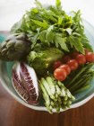 Свіжі овочі в пластиковій тарілці над дерев'яною поверхнею — стокове фото