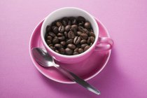 Coffee beans in pink coffee cup — Stock Photo