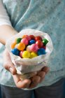 Vista cortada da mão segurando bolas de chiclete coloridas no saco de papel — Fotografia de Stock