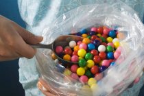 Cropped view of person taking bubble gum balls out of plastic bag with scoop — Stock Photo