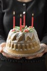Ausgeschnittene Ansicht einer Frau, die Walnuss-Gugelhupf mit vier brennenden Kerzen serviert — Stockfoto