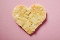 Vista de primer plano de un corazón de pastelería con almendras en copos y azúcar en la superficie rosa - foto de stock