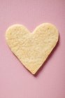 Closeup view of one pastry heart-shaped cookie on pink surface — Stock Photo