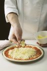 Chef polvilhando pizza com queijo — Fotografia de Stock