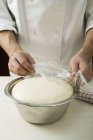 Chef covering pizza dough with clingfilm — Stock Photo