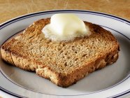 Крупним планом масляний візерунок тане на шматок цільного зернового тосту — стокове фото