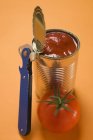 Tomate fresco junto a la lata de comida abierta en la superficie naranja - foto de stock