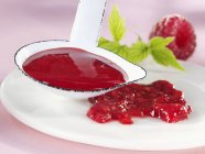 Closeup view of raspberry sauce on plate and in ladle — Stock Photo