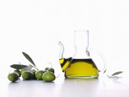 Оливковое масло в графине с зелеными оливками — стоковое фото