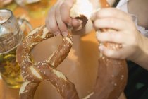 Mani che rompono un pretzel morbido — Foto stock