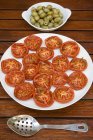 Gebratene Tomaten und eingelegte Oliven auf weißem Teller über hölzerner Oberfläche — Stockfoto